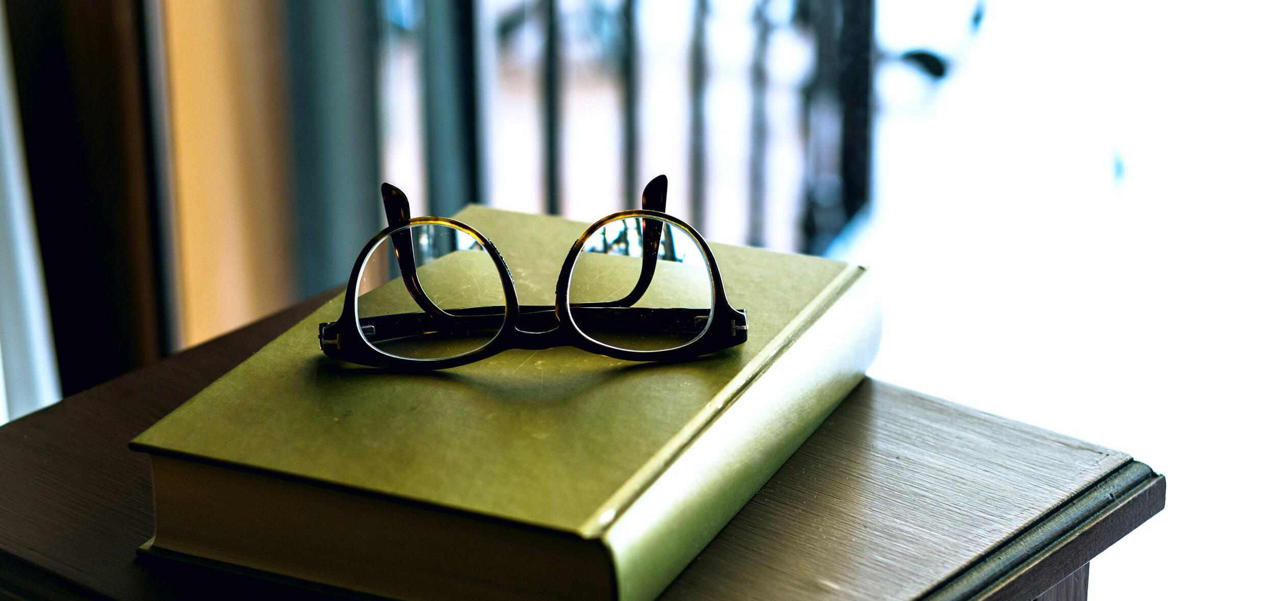 A pile of books with a pair of upside-down eyeglasses on top