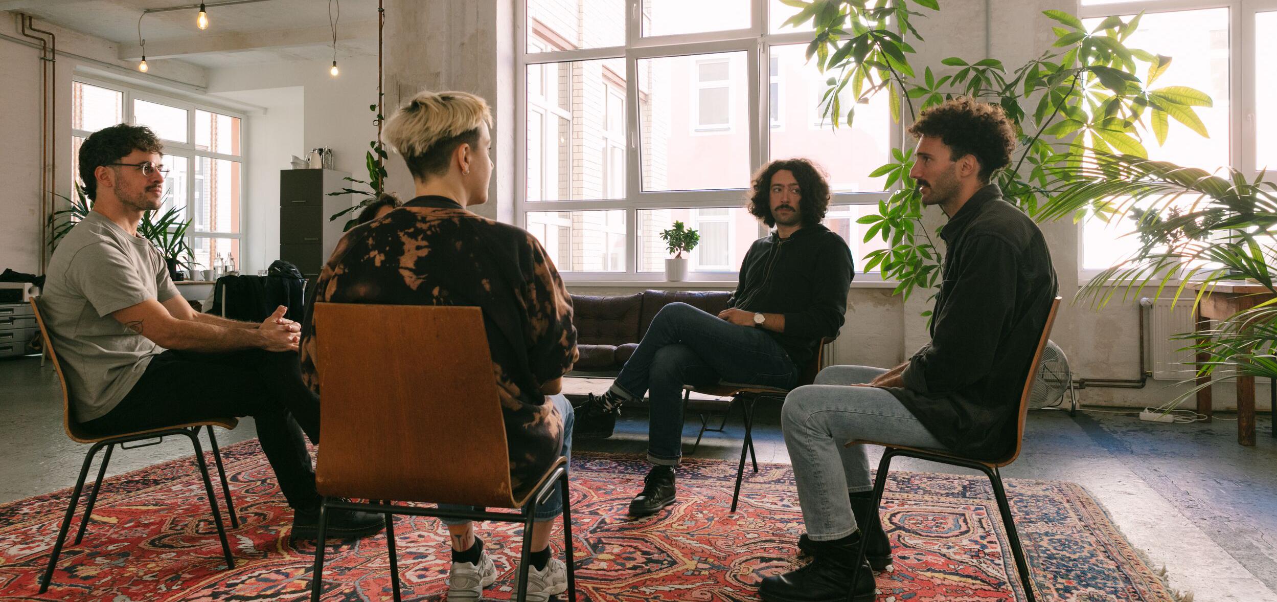 Five people in group therapy sit in discussion in a circle within a bright, airy room