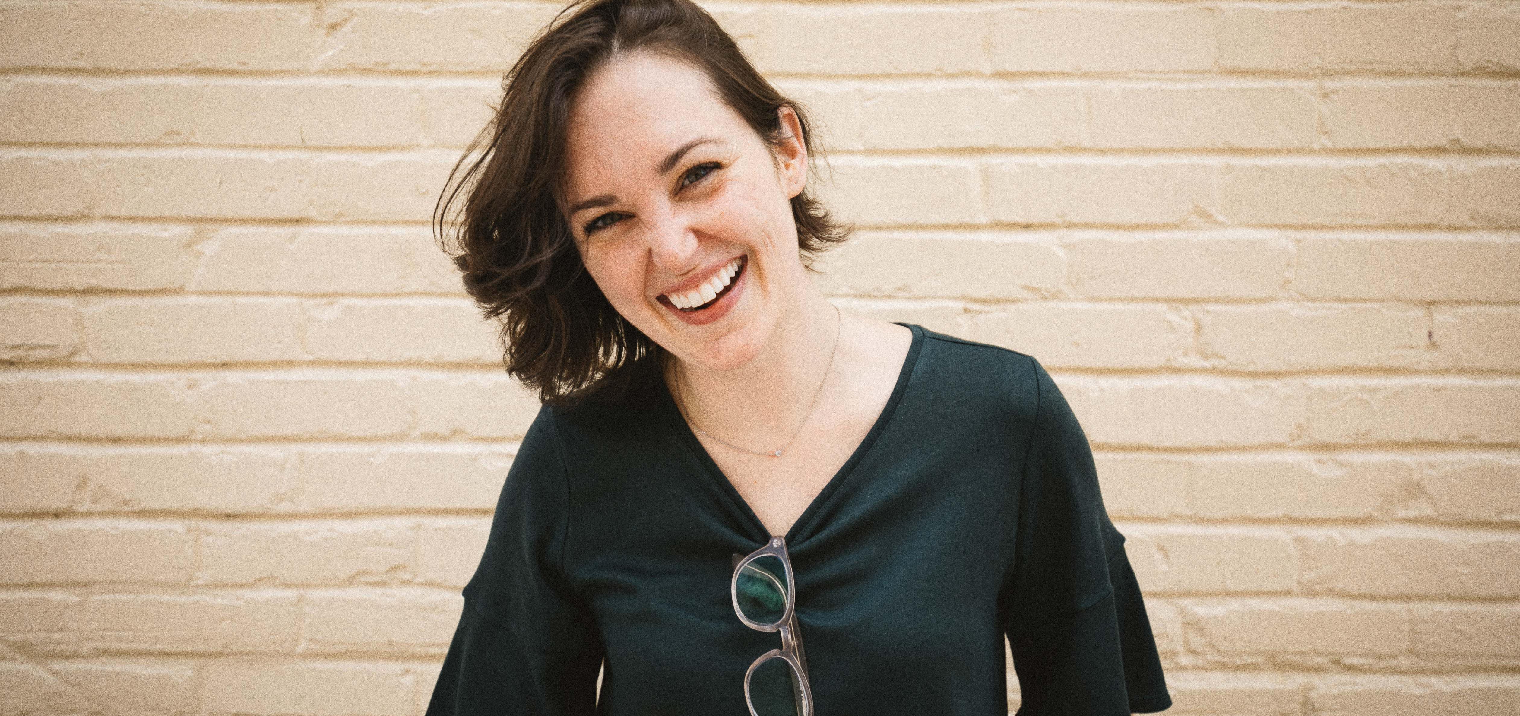 Ahna Crum, R.D.N. smiles in front of beige brick wall in a black t-shirt