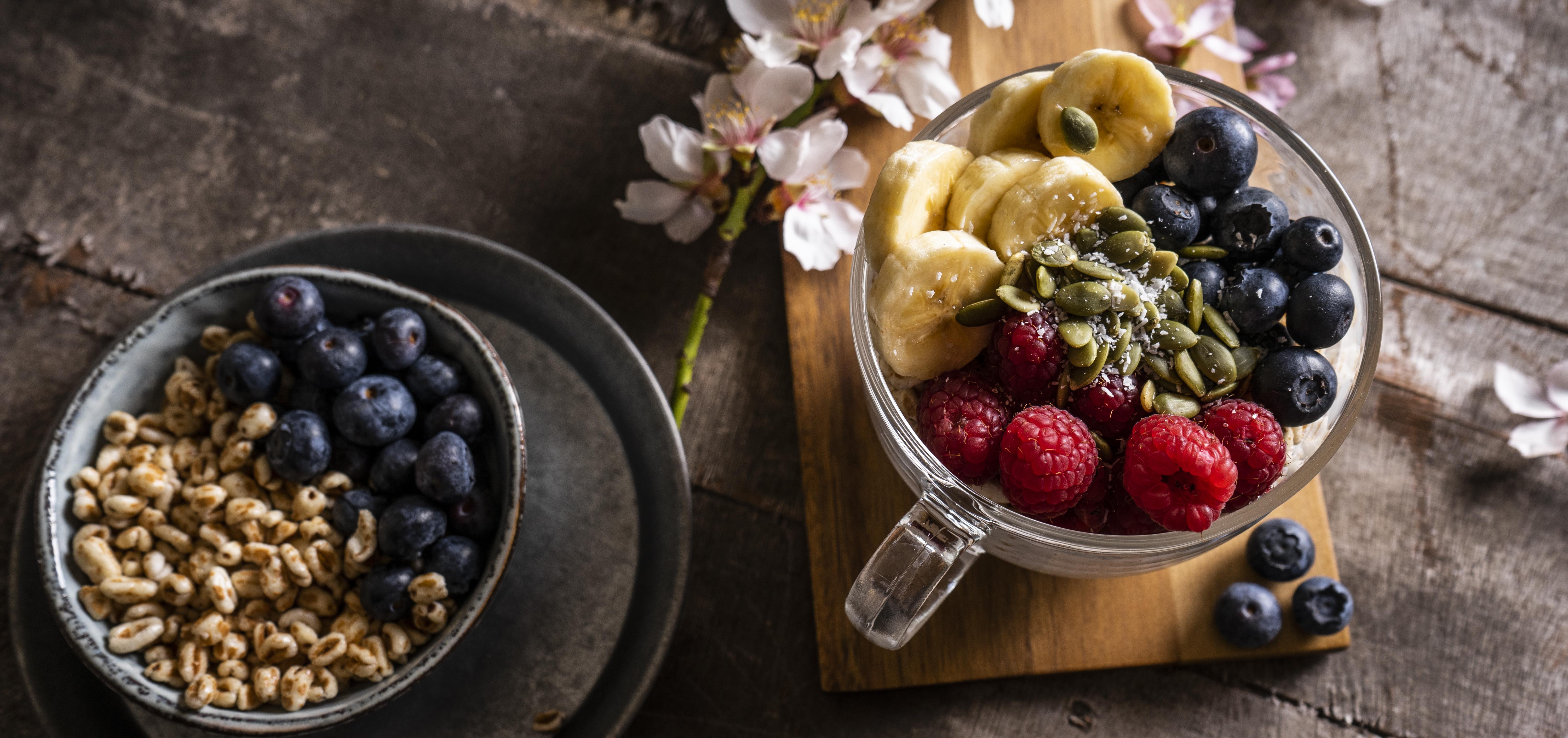 Breakfast bowls with bananas, blueberries, raspberries, walnuts and pumpkin seeds on a rustic wooden surface