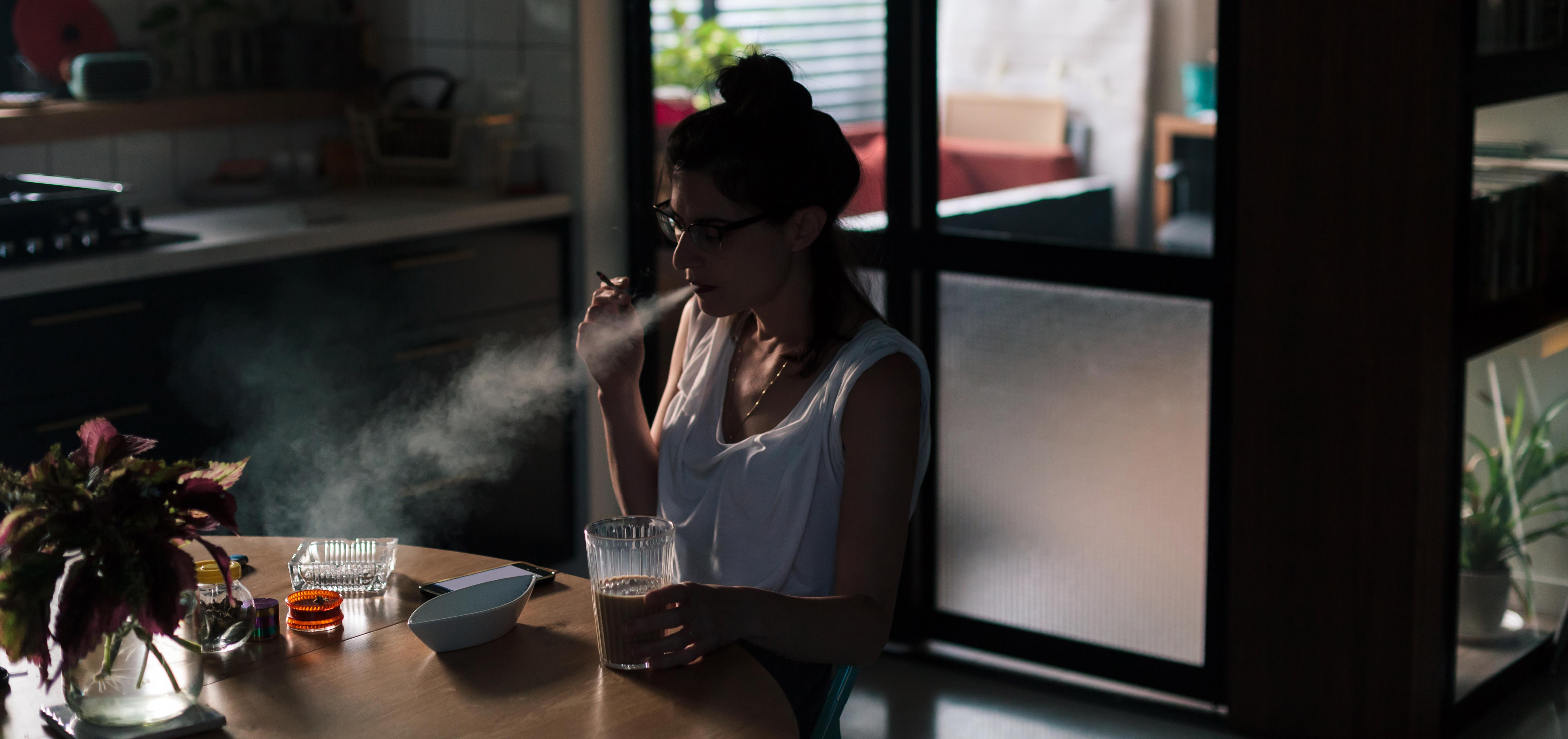 woman sits at the breakfast table exhaling smoke