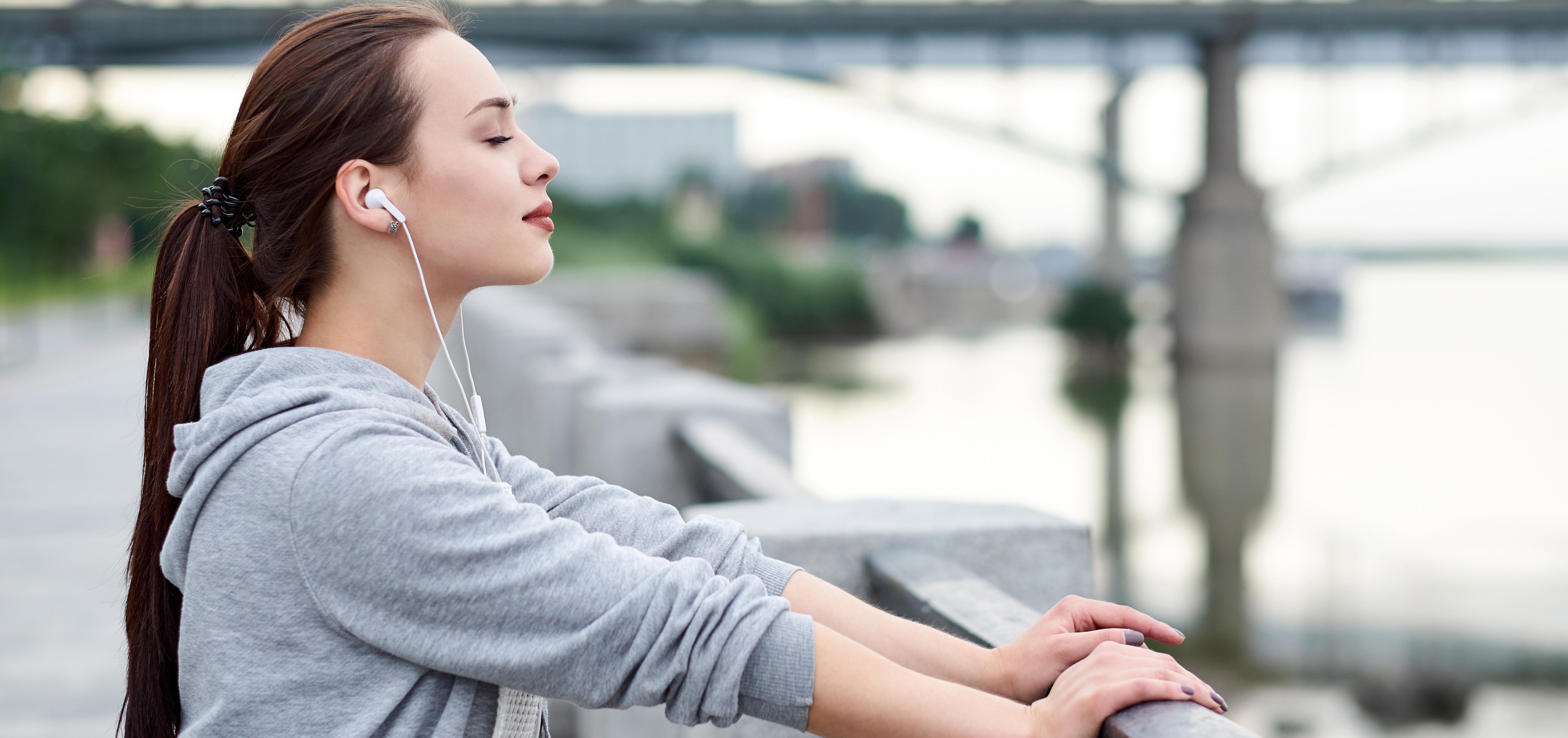 Woman standing with eyes closed, taking a mindful break from a walk along a waterfront.