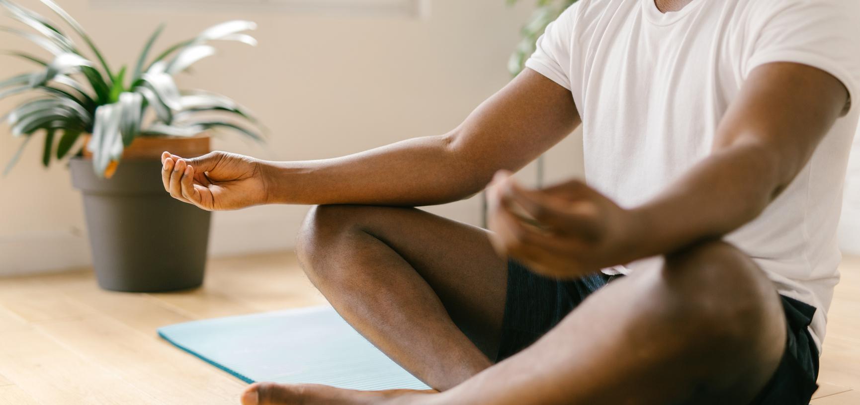 Man sits on a yoga mat, legs crossed, with palms facing up in meditation