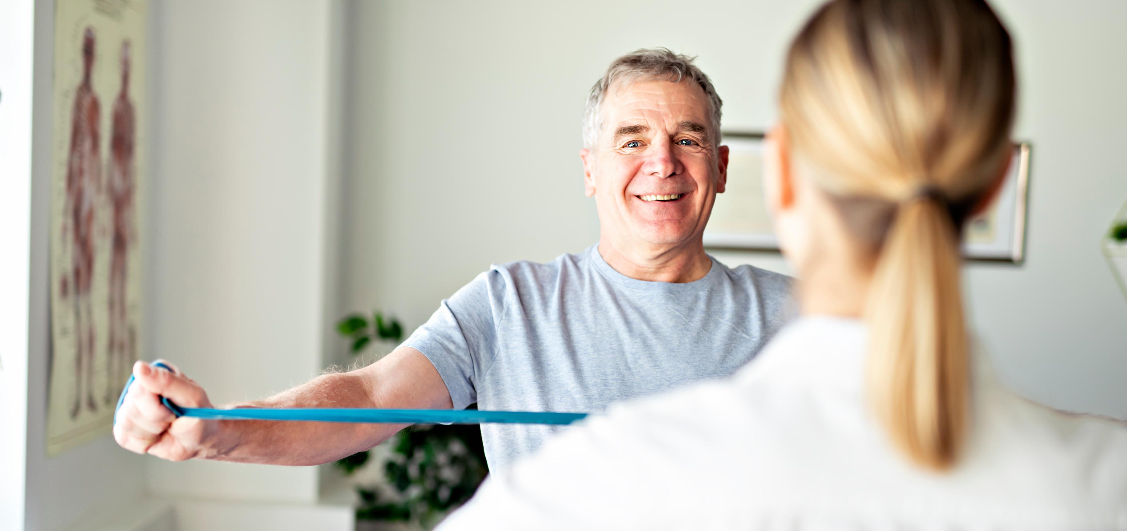 Man standing across from physical therapist, mirroring her exercise instructions