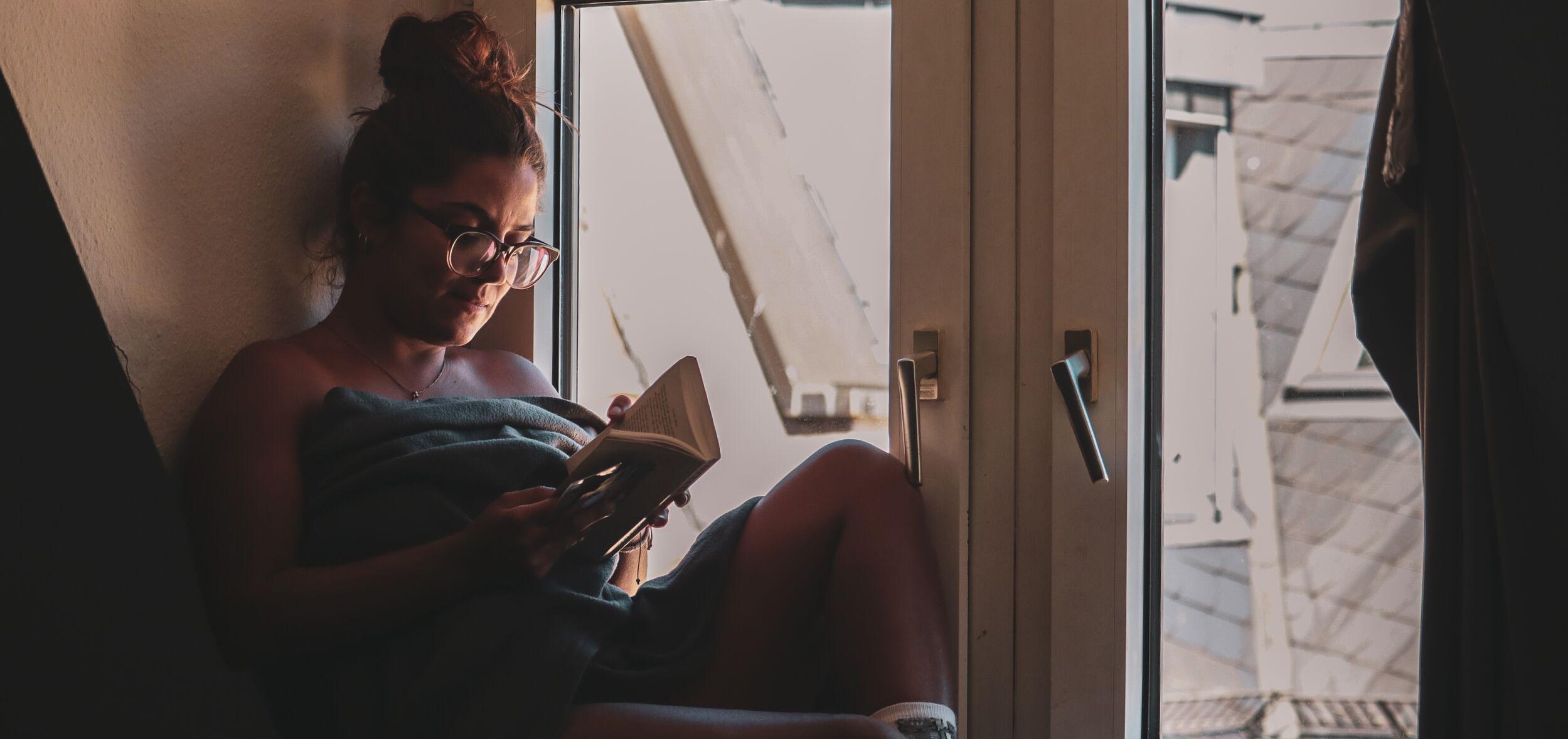 Woman flipping through book pages while sitting on a window bench