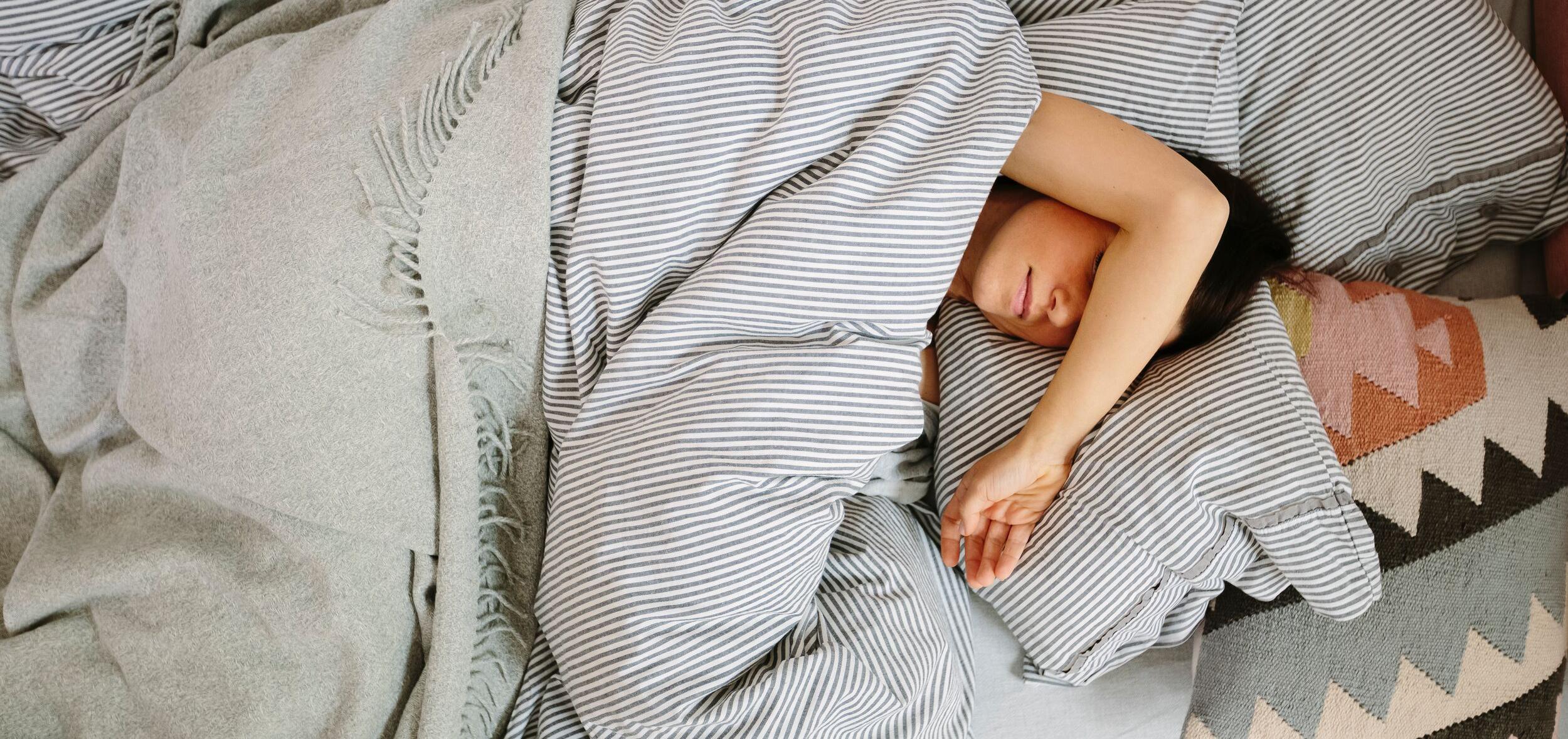 Person asleep in bed under striped sheets