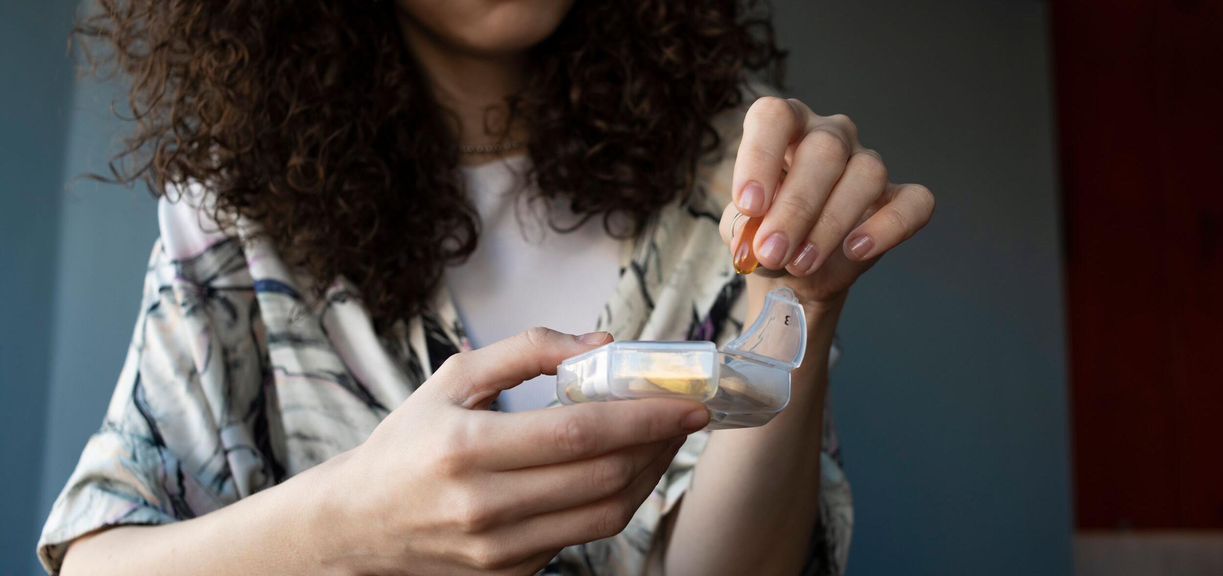 woman taking a vitamin D capsule from a pill box