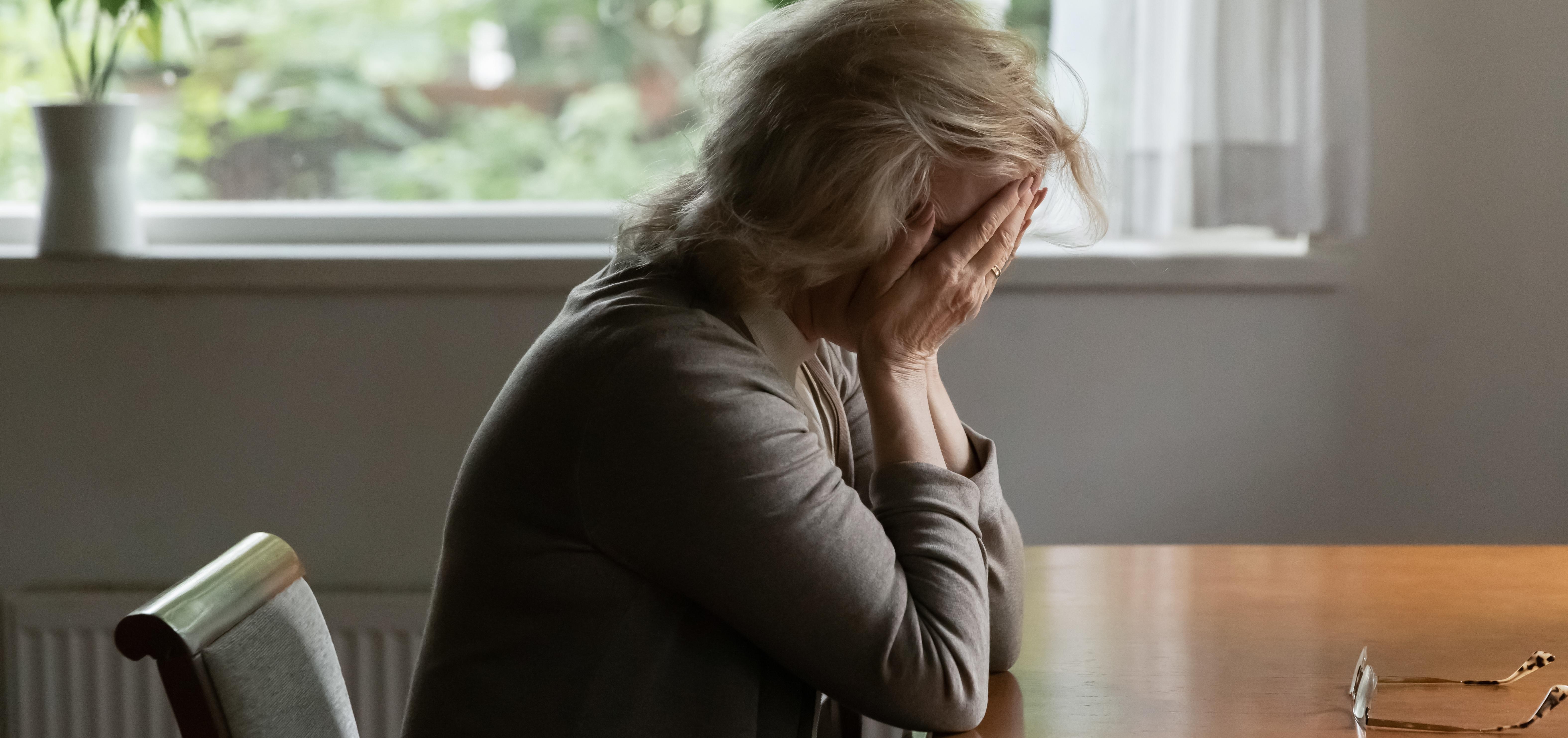 woman sits at a table holding her face in her hands 