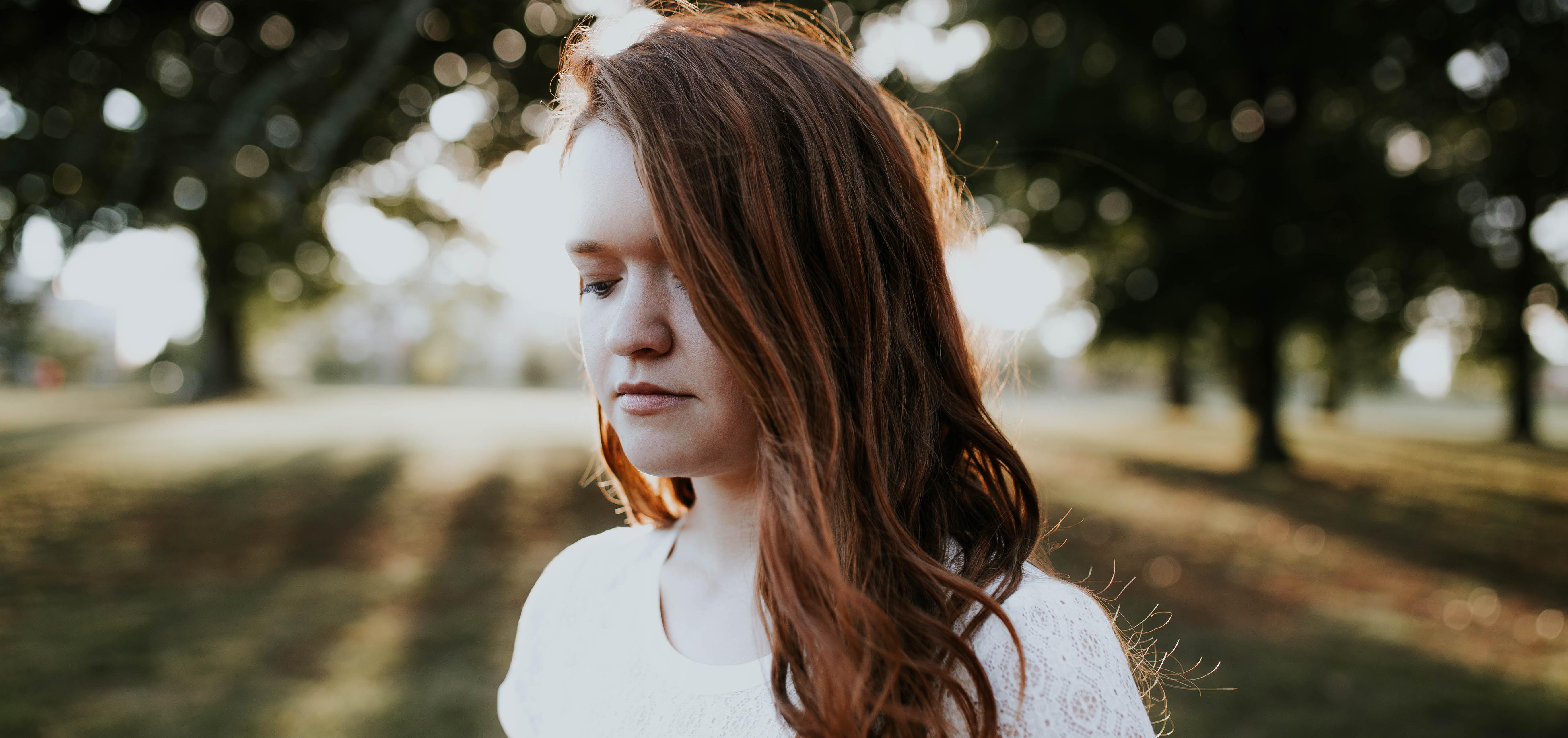 woman in white shirt looks down at ground