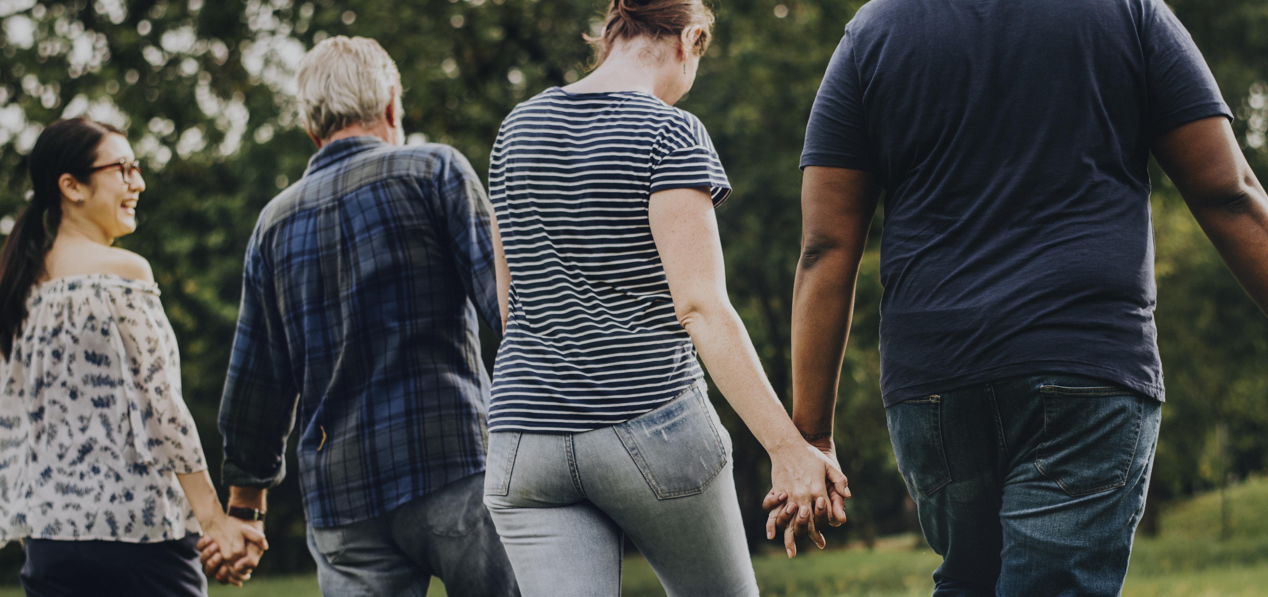 Two couples of various ages hold hands walking through a park