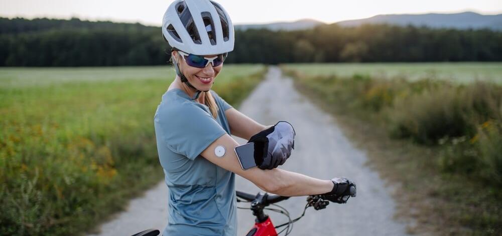 woman on a bike using a continuous glucose monitor (CGM) paired with a smartphone to manage diabetes