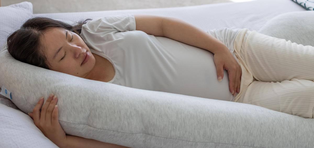 pregnant woman resting her body against a pregnancy pillow