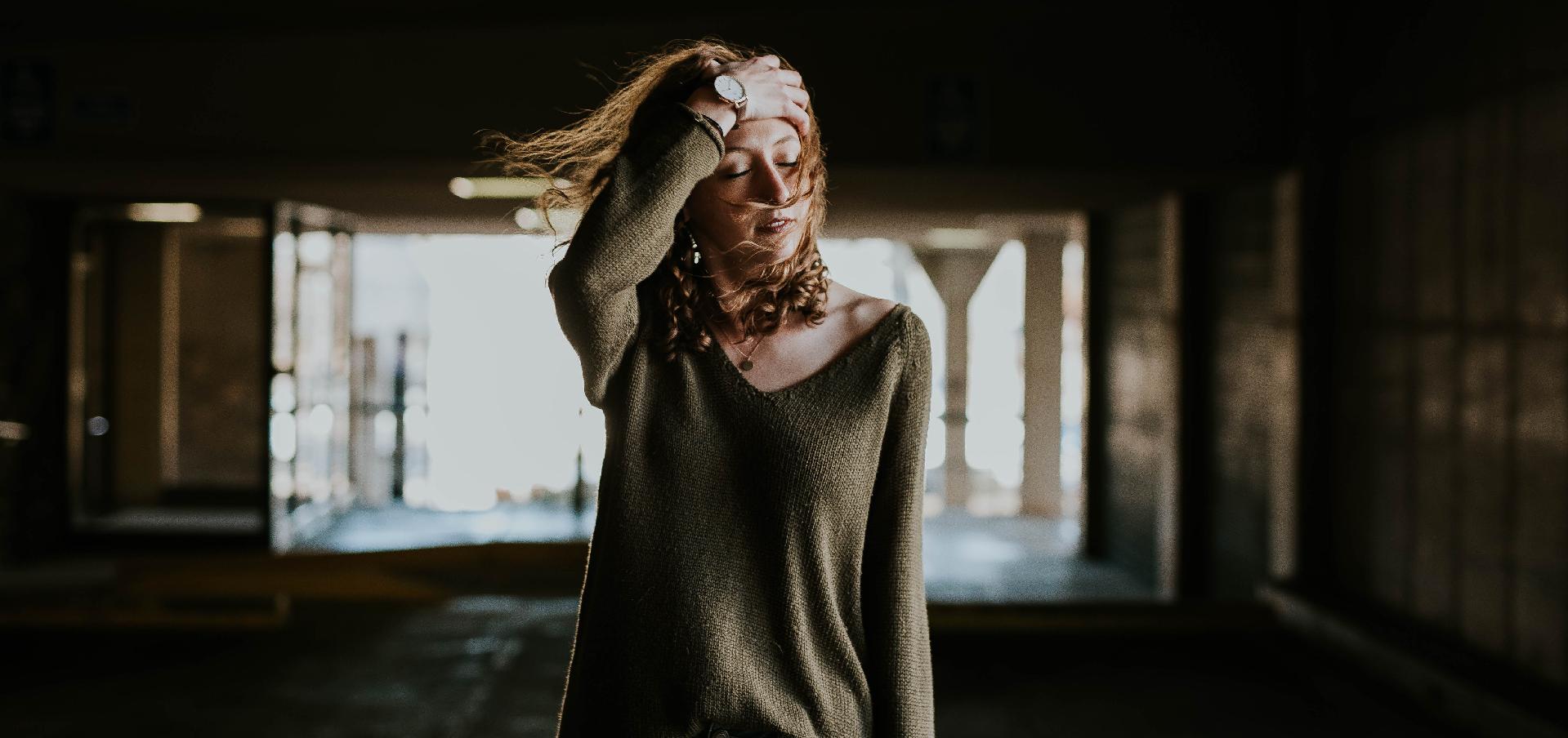 A woman walking on a windy day, pulling her hair out of her face and appearing stressed