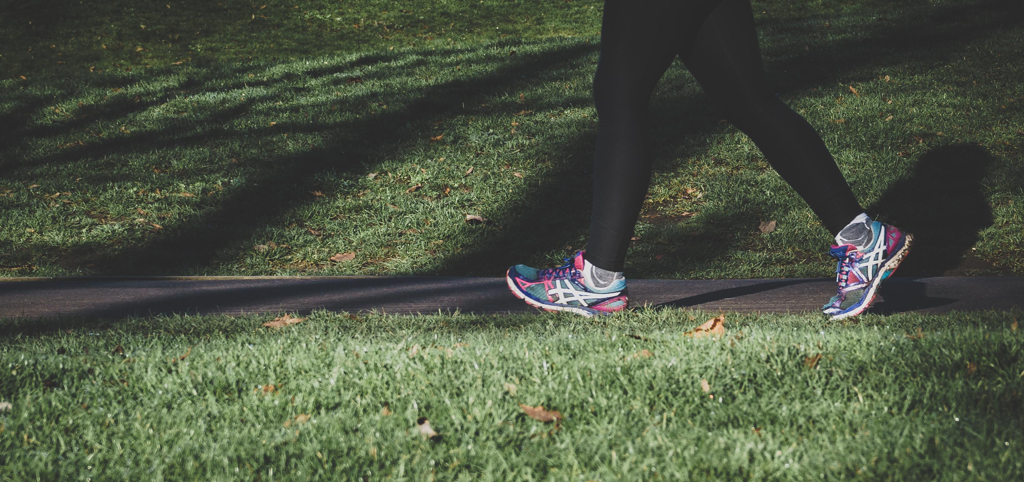 A person wearing black leggings and colorful running sneakers walking in a grassy park to make exercise a hobby