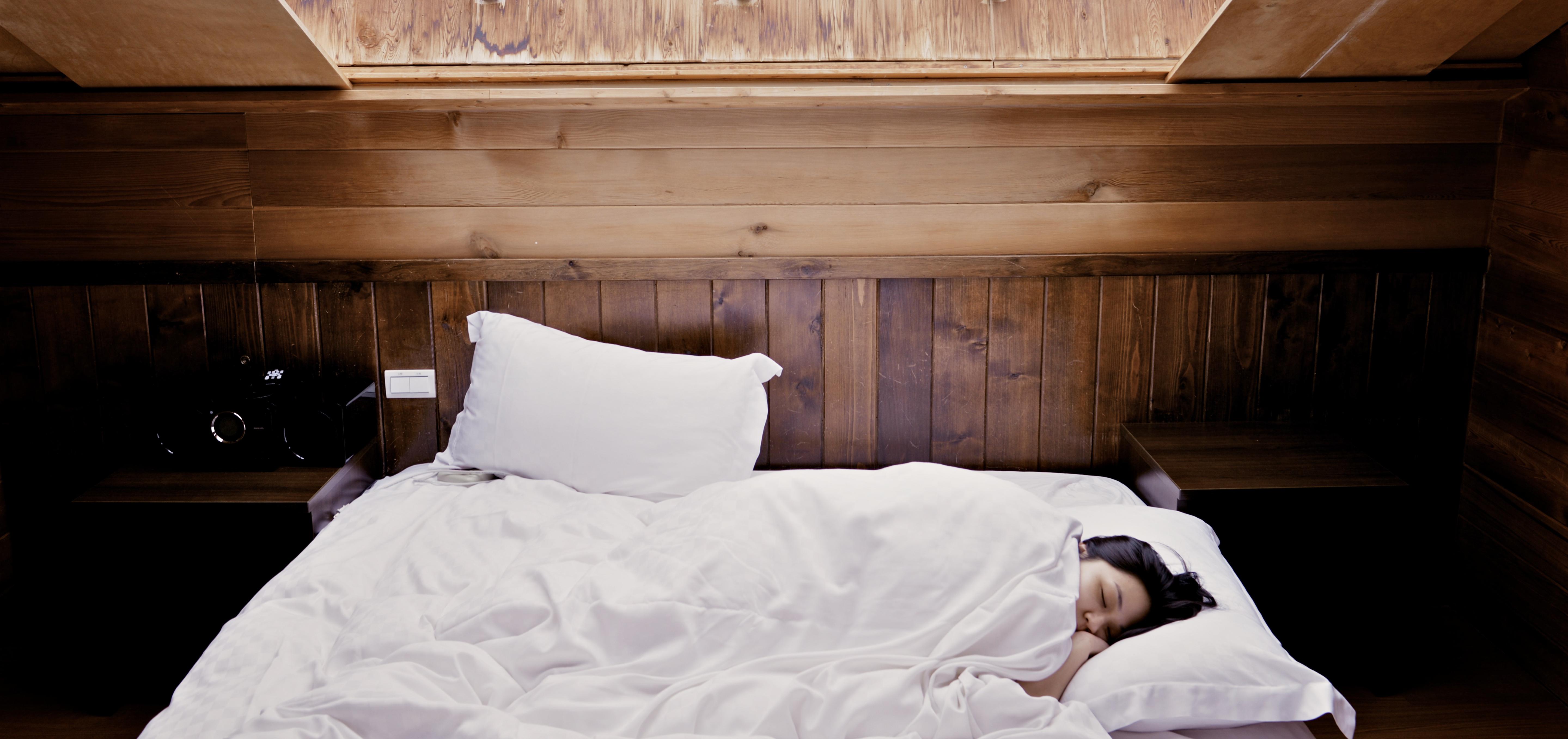 A woman snuggled up in bed with white linens