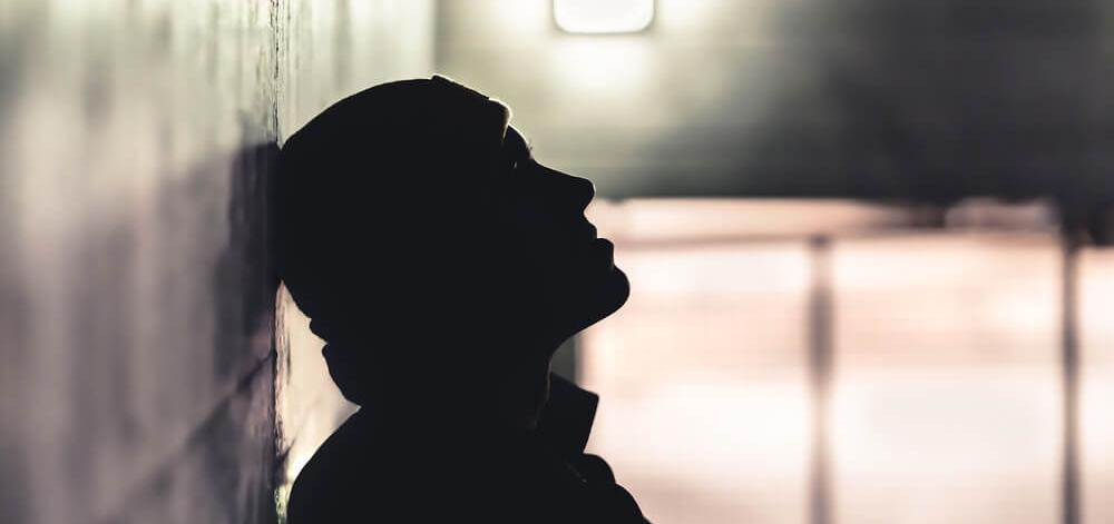 person in a shadowy room, leaning their head against the wall