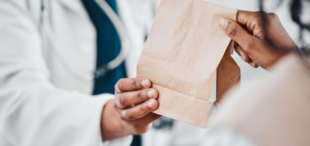 Pharmacist handing a person their prescription medication in a paper bag