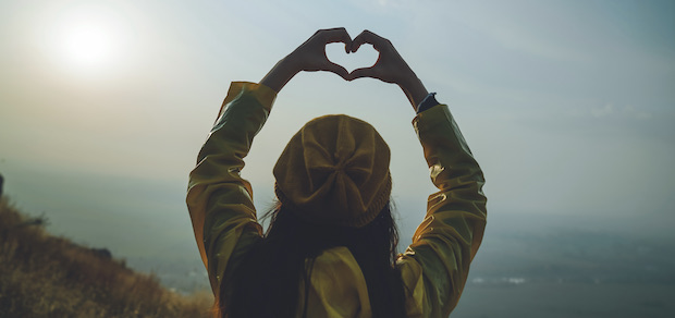 woman looking out over a scenic view with her hands in a heart shape